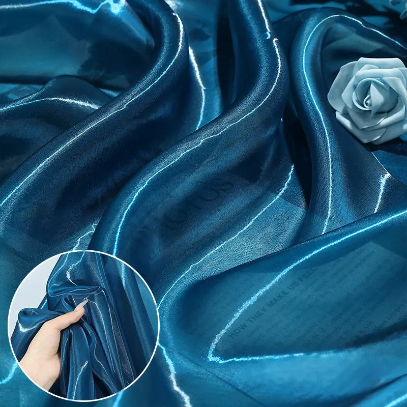 Longan Craft's Shiny Liquid Organza Fabric by the Yard features a colorful glossy finish, shown in soft blue folds with a matching artificial rose—perfect for luxury gowns. Inset: A hand displays the fabric's lustrous texture and sheen.