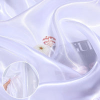 Shiny Liquid Organza Fabric by the yard from Longan Craft drapes smoothly in a sheer white with a colorful glossy finish; seashell and magazine details show its translucency—ideal for luxury bridal gowns.