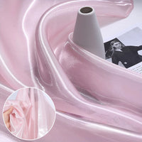 Shiny Liquid Organza Fabric by the yard from Longan Craft, shown in light pink draped on a white spool. This luxury, glossy finish organza textile is ideal for elegant bridal or evening gowns. Inset shows fingers holding the sheer material.