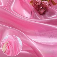 Longan Craft's Shiny Liquid Organza Fabric by the yard features a colorful, glossy finish. Perfect for luxury gowns or evening wear, this silky organza drapes beautifully—shown here with pink roses and a hand gathering its smooth texture.