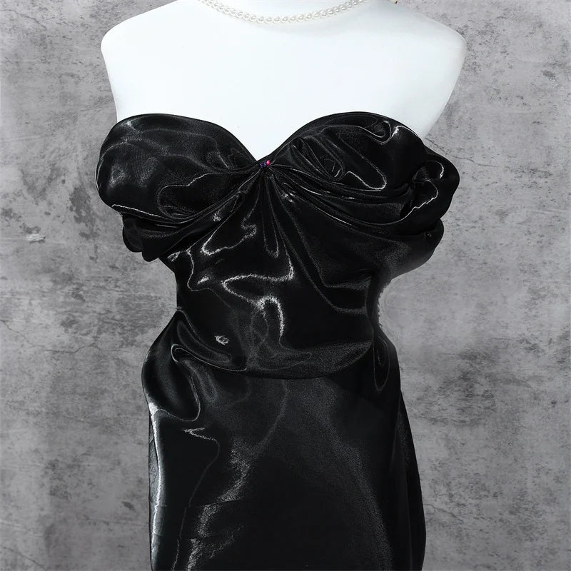 A mannequin displays a strapless evening dress made from Longan Craft's Shiny Liquid Organza Fabric By The Yard, featuring a colorful glossy finish and ruched details that enhance its fitted silhouette against a gray textured background.