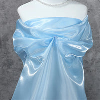 A mannequin displays Longan Craft's Shiny Liquid Organza Fabric by the yard, a colorful glossy finish textile ideal for luxury gowns. Draped with a large bow and paired with a pearl necklace, it stands against a textured gray backdrop.