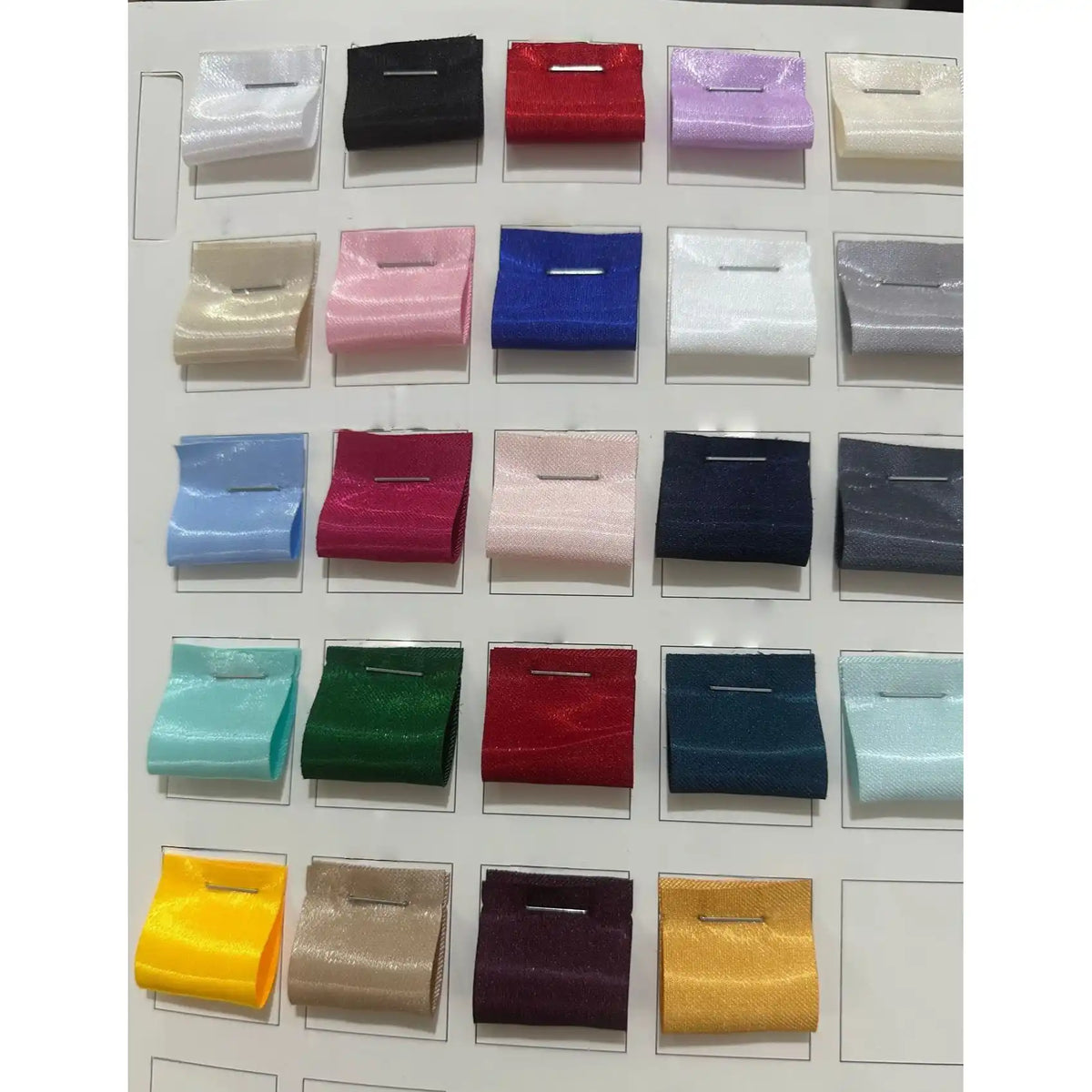 A display card from Longan Craft shows 24 neatly arranged rectangular swatches of Shiny Liquid Satin Fabric By The Yard in assorted solid colors, each pinned in place—perfect for formalwear and bridesmaid dresses.