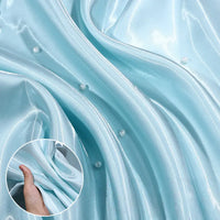 Close-up of Longan Craft’s Shiny Liquid Satin Fabric By The Yard in light blue with pearl accents. An inset displays a hand gathering the glossy polyester satin, highlighting its luxurious texture—ideal for formalwear and bridesmaid dresses.