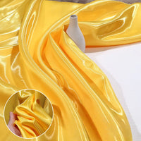 Shiny Liquid Satin Fabric By The Yard from Longan Craft in a solid yellow color is draped beside a small white vase, with an inset showing a hand pinching the smooth, lustrous material—ideal for bridesmaid dresses and formalwear.
