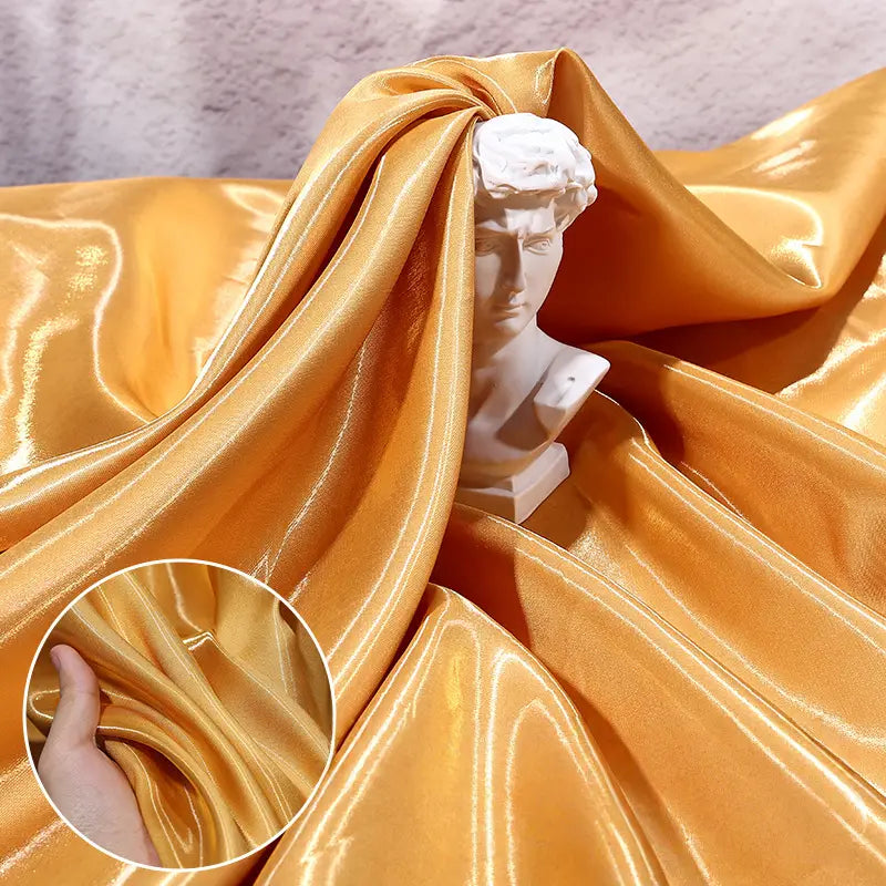 A small white bust sculpture is partly wrapped in Longan Craft’s Shiny Liquid Satin Fabric By The Yard, with a hand pinching the smooth, lustrous satin to showcase its elegant texture—ideal for bridesmaid dresses and formalwear.