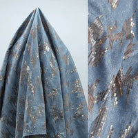 A close-up of Longan Craft’s Shiny Sequin Embroidered Denim Fabric shows cotton-embroidered washed denim by the yard with bronze and silver sequins; left side draped, right side highlights detailed sequin design. Great for dress, skirt, or coat.
