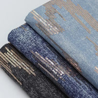 Three folded pieces of Longan Craft’s Shiny Sequin Embroidered Denim Fabric by the yard, in black, blue, and light blue washed denim with cotton embroidery and gold sequin abstract patterns for dress, skirt, or coat.
