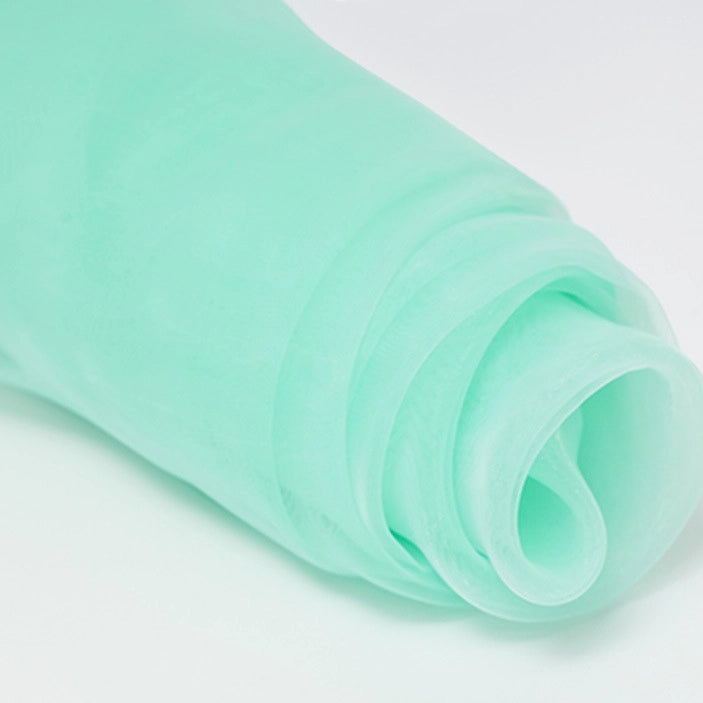 A close-up of Longan Craft’s Silky Polyester Organza Fabric by the Yard—premium, soft, and sheer bridal organza material in a solid light green color—rolled up on a white surface.