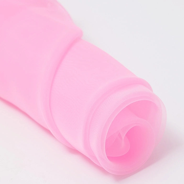 A close-up of Longan Craft's Silky Polyester Organza Fabric By The Yard shows its soft, sheer texture in light pink—premium solid color organza ideal for bridal gowns or evening dresses, partially unrolled on a white surface.