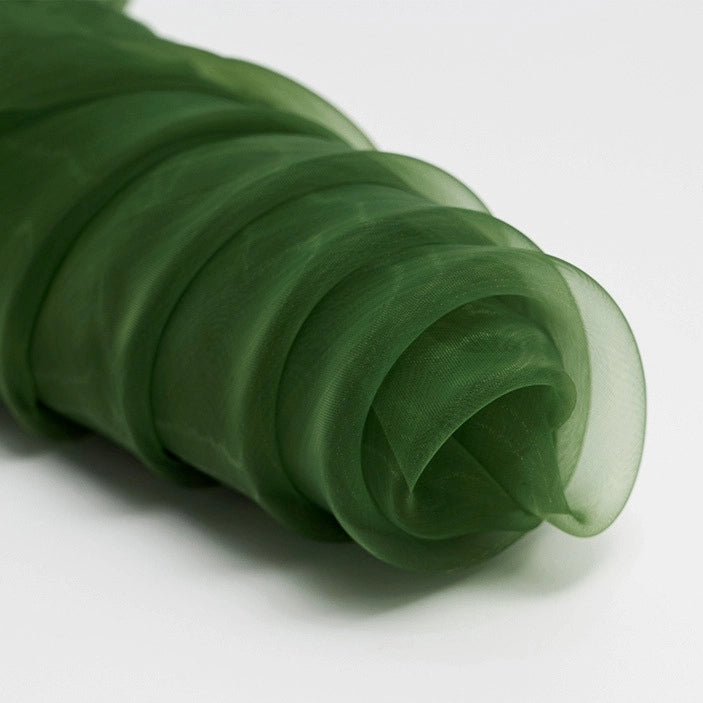 Longan Craft's Silky Polyester Organza Fabric By The Yard is a premium, soft, and sheer organza in dark green, shown loosely gathered on a white surface—ideal for evening dresses or elegant bridal gowns.