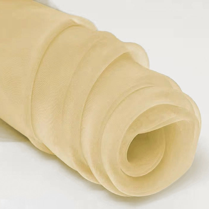 A close-up of Longan Craft's Silky Polyester Organza Fabric By The Yard, a premium soft and sheer bridal organza material in beige, perfect for evening dresses or gowns, shown rolled up on a light surface.