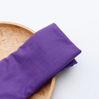 A piece of Longan Craft Single Jersey Fabric By The Yard, a colorful polyester jersey cloth for casual wear, is folded on a round woven bamboo tray against a white background.