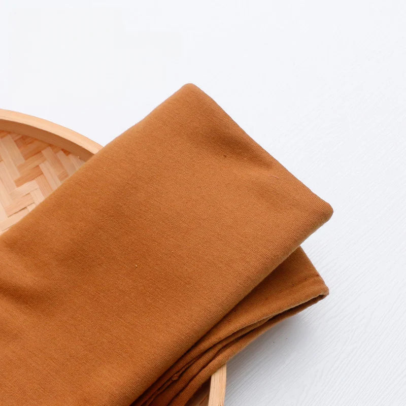 A piece of colorful Single Jersey Fabric by the yard from Longan Craft lies folded in a round, light wooden basket on a white surface. This breathable polyester jersey material is ideal for casual wear and various crafting projects.