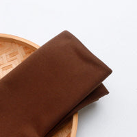 A piece of Longan Craft Single Jersey Fabric By The Yard, colorful polyester jersey material for casual wear, is folded on the edge of a round woven bamboo tray against a white background.