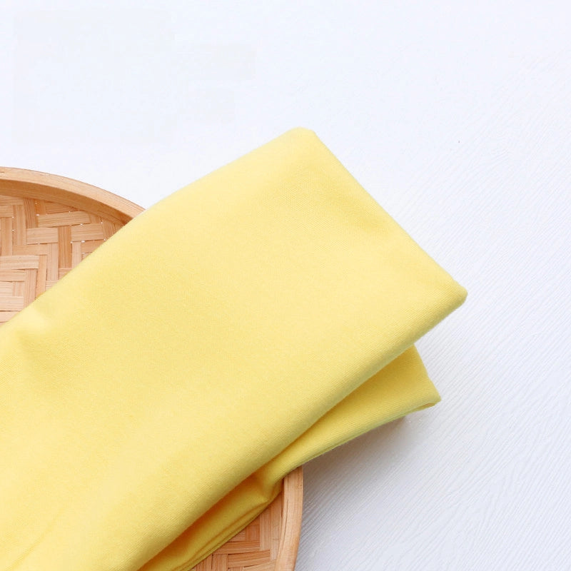 A piece of Longan Craft Single Jersey Fabric By The Yard in bright yellow polyester blend is displayed on a round bamboo tray against a white background.