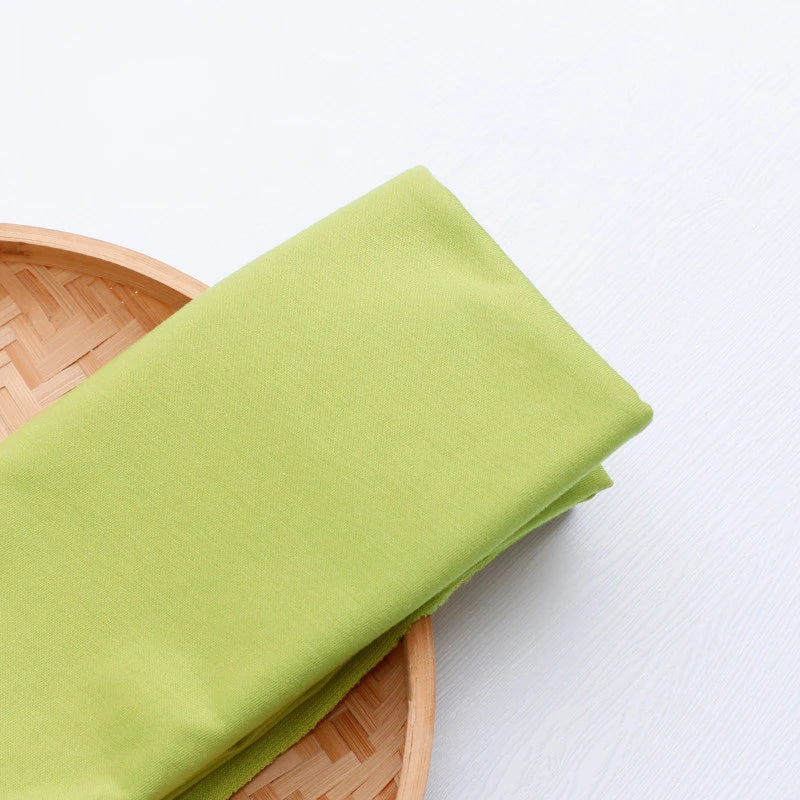 A folded piece of Longan Craft Single Jersey Fabric By The Yard—colorful polyester jersey cloth for casual wear—rests on a round, woven bamboo tray placed on a white surface.