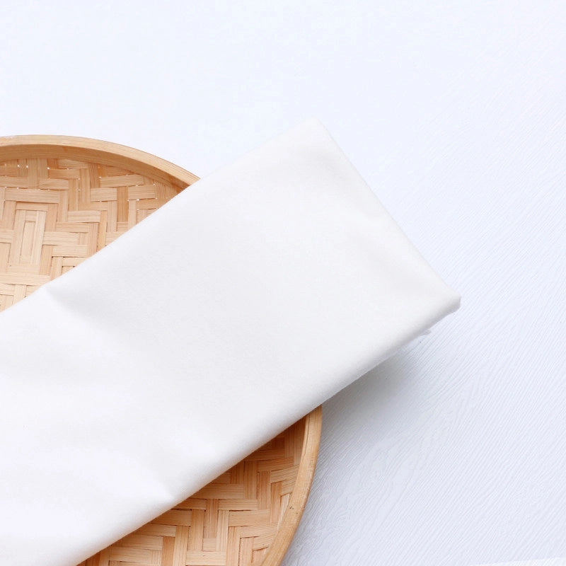 A piece of colorful Longan Craft Single Jersey Fabric by the Yard, made from moisture-wicking polyester jersey material for casual wear, is neatly folded on a round woven bamboo tray against a white background.