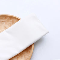 A piece of colorful Longan Craft Single Jersey Fabric by the Yard, made from moisture-wicking polyester jersey material for casual wear, is neatly folded on a round woven bamboo tray against a white background.