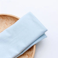 A Single Jersey Fabric by the Yard from Longan Craft in light blue polyester rests folded on a round bamboo tray, displayed against a white background—ideal jersey cloth material for casual wear.