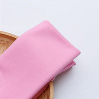 A piece of Longan Craft Single Jersey Fabric By The Yard in light pink rests neatly folded on a round bamboo tray, showcasing this colorful polyester jersey cloth material for casual wear.