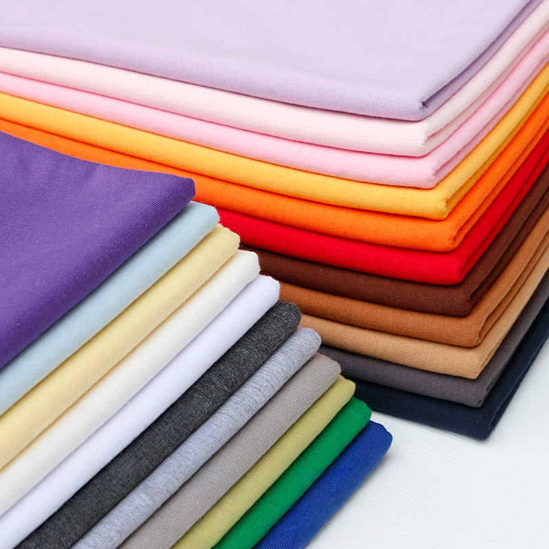 Stacks of Longan Craft Single Jersey Fabric By The Yard—colorful polyester jersey cloth for casual wear—neatly folded in solid shades like purple, orange, pink, red, and more on a flat surface.