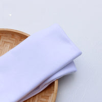 A colorful polyester single jersey fabric by the yard from Longan Craft rests folded on a round bamboo tray placed on a light-colored surface.