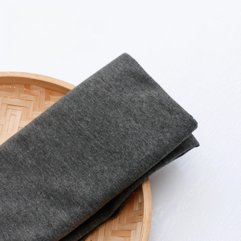 A piece of colorful polyester single jersey fabric by the yard from Longan Craft is displayed folded on a round, woven bamboo tray against a white background—ideal jersey cloth material for casual wear.