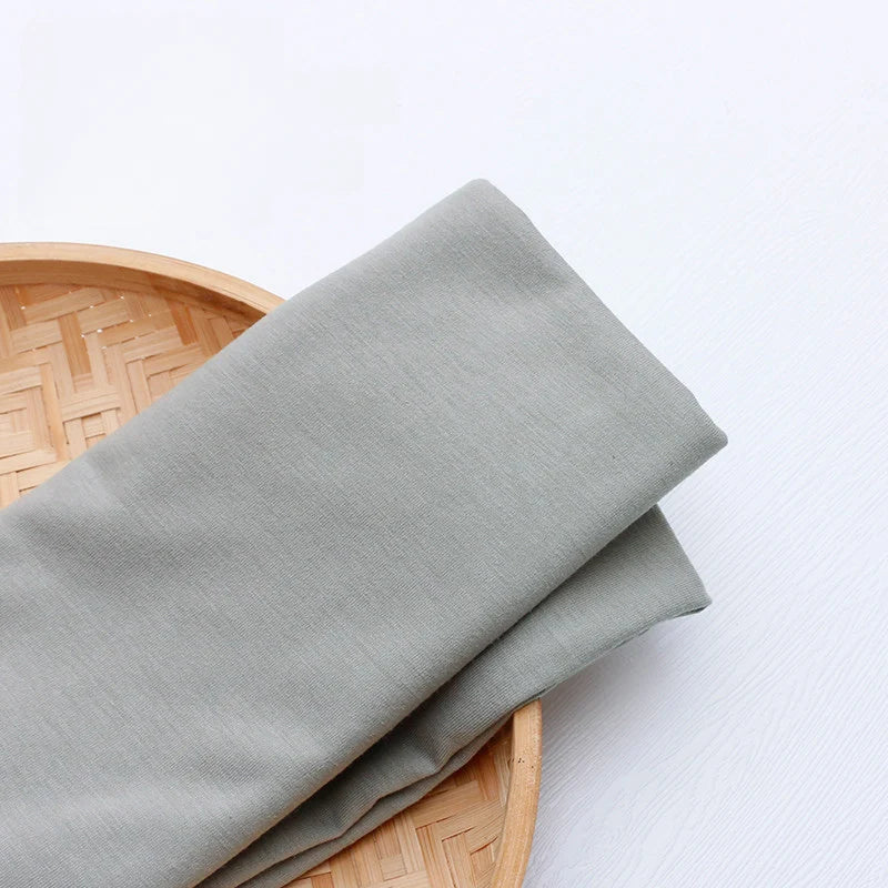 A piece of Longan Craft Single Jersey Fabric By The Yard in colorful polyester rests folded on a round bamboo tray placed on a white surface, perfect as jersey cloth material for casual wear.