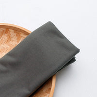 A neatly folded piece of Longan Craft’s Single Jersey Fabric By The Yard in dark gray polyester is displayed on a round bamboo tray, ideal for casual wear and featured as colorful jersey cloth material.