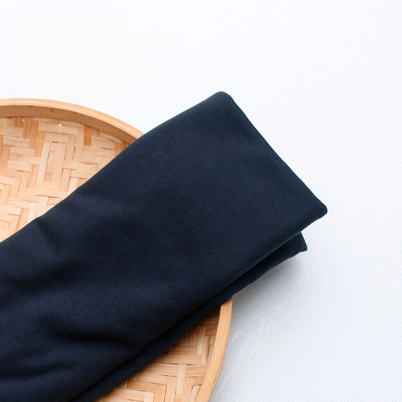 A yard of colorful polyester jersey fabric from Longan Craft is neatly folded on a round, woven bamboo tray against a white background, perfect for creating casual wear.