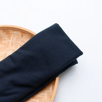 A yard of colorful polyester jersey fabric from Longan Craft is neatly folded on a round, woven bamboo tray against a white background, perfect for creating casual wear.