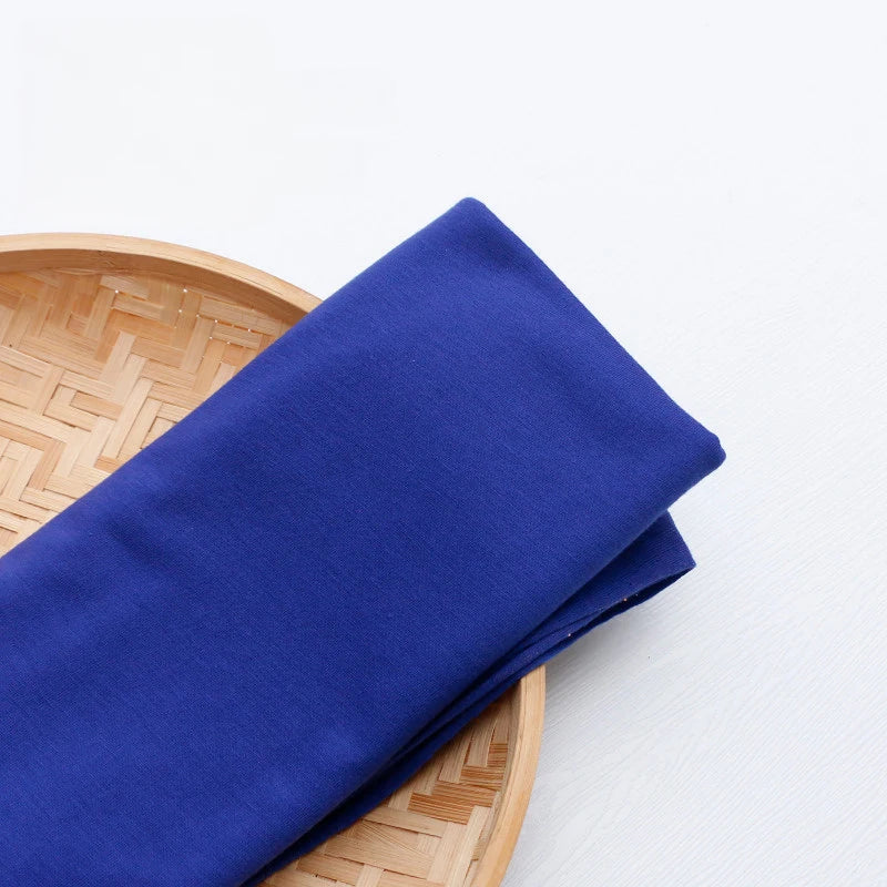 A piece of Longan Craft Single Jersey Fabric by the yard in royal blue polyester rests on a round, woven bamboo tray, perfect for colorful casual wear and sewing projects.
