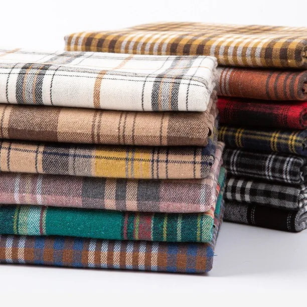 A neatly arranged stack of Longan Craft Single Sided Sueded Plaid Flannel Fabric By The Yard—featuring medium weight polyester cotton flannel in a variety of plaid patterns and colors such as beige, white, green, red, and black—is displayed on a white background. This premium soft flannel clothing material is perfect for projects requiring high-quality plaid flannel by the yard.