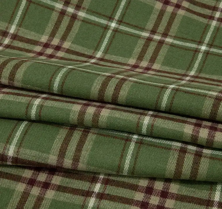 The Single Sided Sueded Plaid Flannel Fabric By The Yard from Longan Craft is a medium weight polyester cotton textile featuring a green and brown checkered pattern, with intersecting lines in shades of green, beige, and brown. This premium soft flannel clothing material is brushed for warmth and comfort, making it ideal for cozy projects. The neatly folded fabric showcases its appealing sueded texture and classic plaid design.