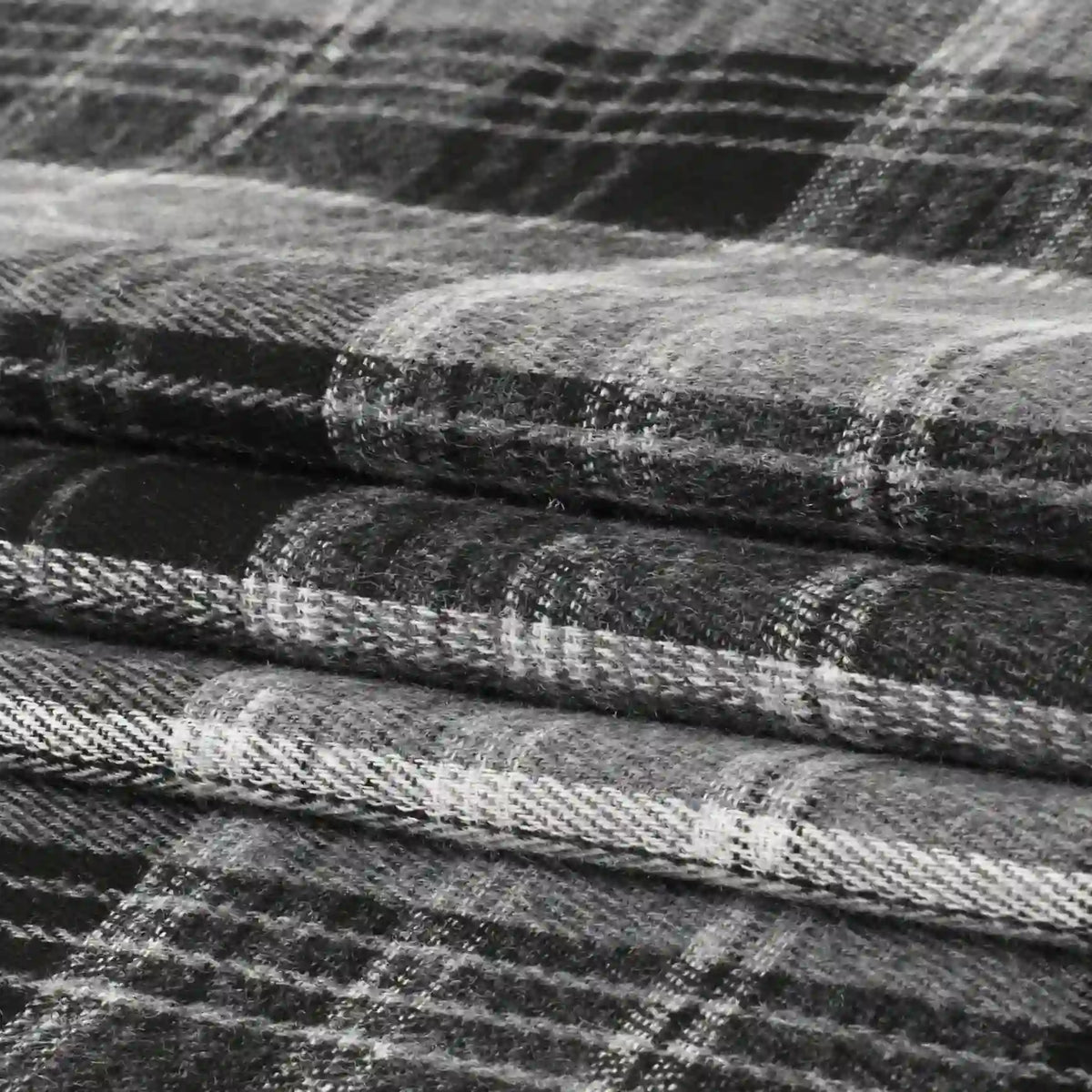 Neatly stacked in three layers, the Longan Craft Single Sided Sueded Plaid Flannel Fabric By The Yard features a classic black, white, and gray checkered pattern. This premium soft medium-weight polyester cotton flannel textile boasts a sueded finish for a cozy texture—perfect for clothing and craft projects.