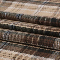 A close-up of folded Longan Craft Single Sided Sueded Plaid Flannel Fabric By The Yard displays detailed woven texture and horizontal lines in shades of brown, beige, and black. This medium weight polyester cotton flannel textile features a premium sueded finish, emphasizing the softness and warmth ideal for clothing material purchased by the yard.