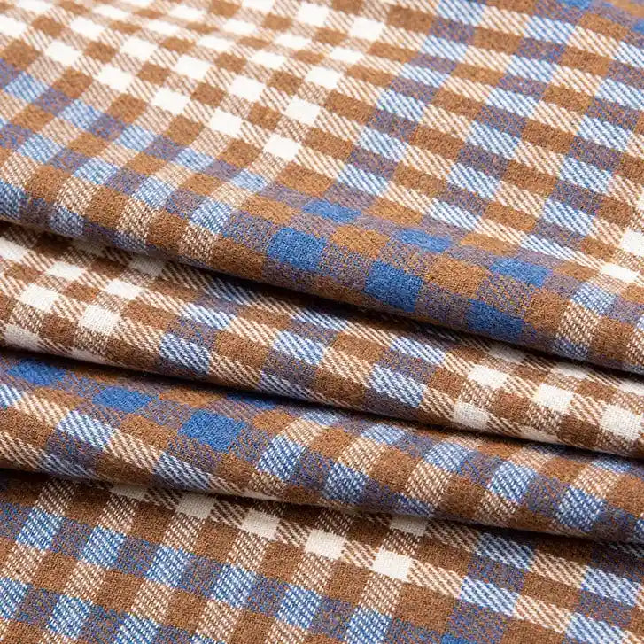 The Single Sided Sueded Plaid Flannel Fabric by the yard from Longan Craft features a premium soft, medium weight polyester cotton blend with a brown, blue, and white checkered pattern. The fabric is neatly folded in overlapping layers, showcasing its soft flannel texture—ideal for clothing and crafts.