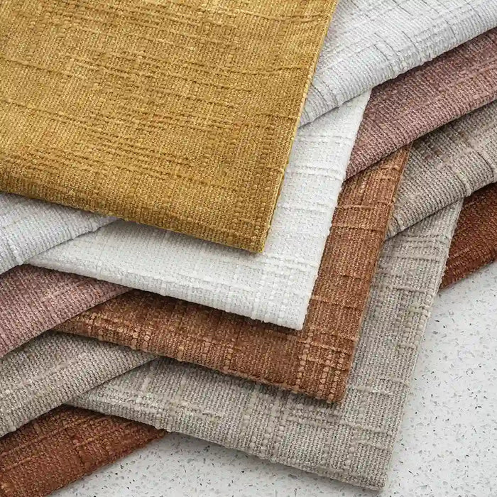 Swatches of Longan Craft's Slub Textured Chenille Fabric By The Yard in solid neutral tones—mustard yellow, white, beige, light brown, tan, and gray—are arranged in a fan shape on a speckled surface.