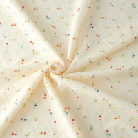 Small Floral Printed Swiss Dot Fabric by Longan Craft features cozy cream cotton with a dotted texture, accented by tiny red, blue, green, and yellow floral prints. Perfect for clothing; fabric shown elegantly swirled.