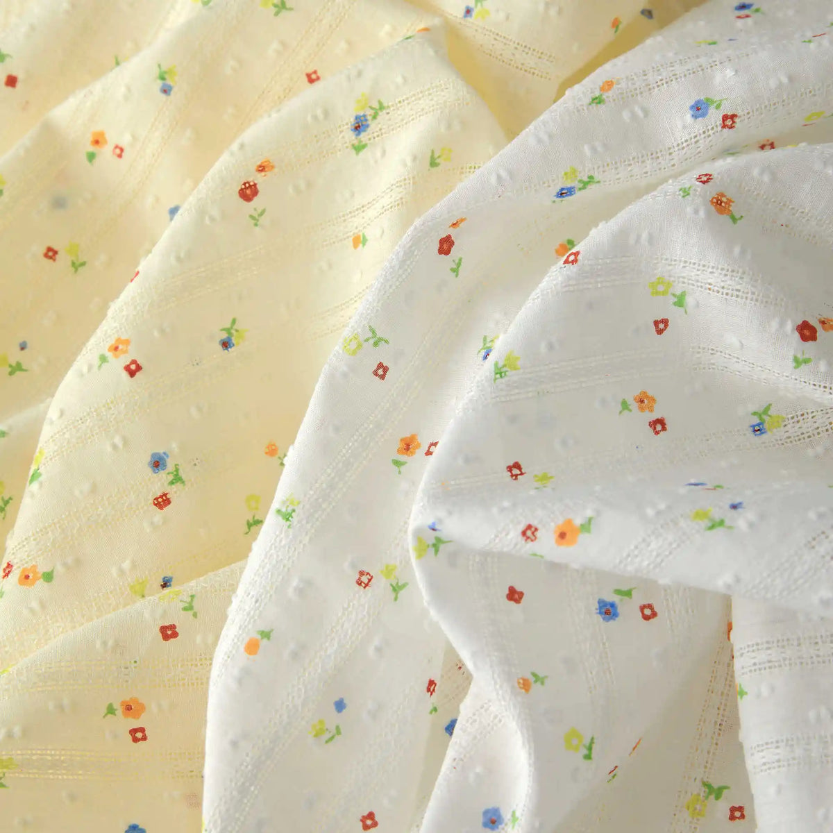 Close-up of Longan Craft’s Small Floral Printed Swiss Dot Fabric By The Yard—cozy cotton material with a subtle checkered texture, airy drape, and colorful floral prints on white and pale yellow backgrounds.