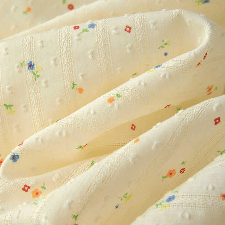 Longan Craft’s Small Floral Printed Swiss Dot Fabric by the yard features cozy cream-colored cotton with blue, red, and orange floral prints and a textured dotted pattern—perfect for clothing and crafts.