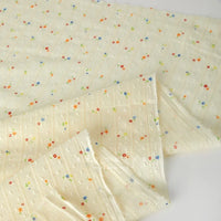 Longan Craft’s Small Floral Printed Swiss Dot Cotton Fabric features thin textured stripes and scattered red, blue, green, and orange flowers on cream, ideal for clothing. Sold by the yard; some edges are shown folded over.