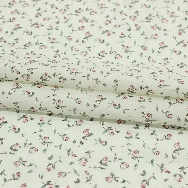 Longan Craft's Small Floral Printed Voile Fabric by the yard is 100% cotton with a botanical pattern of small pink roses and green leaves on a white background—perfect as a soft, lightweight material for summer clothing.