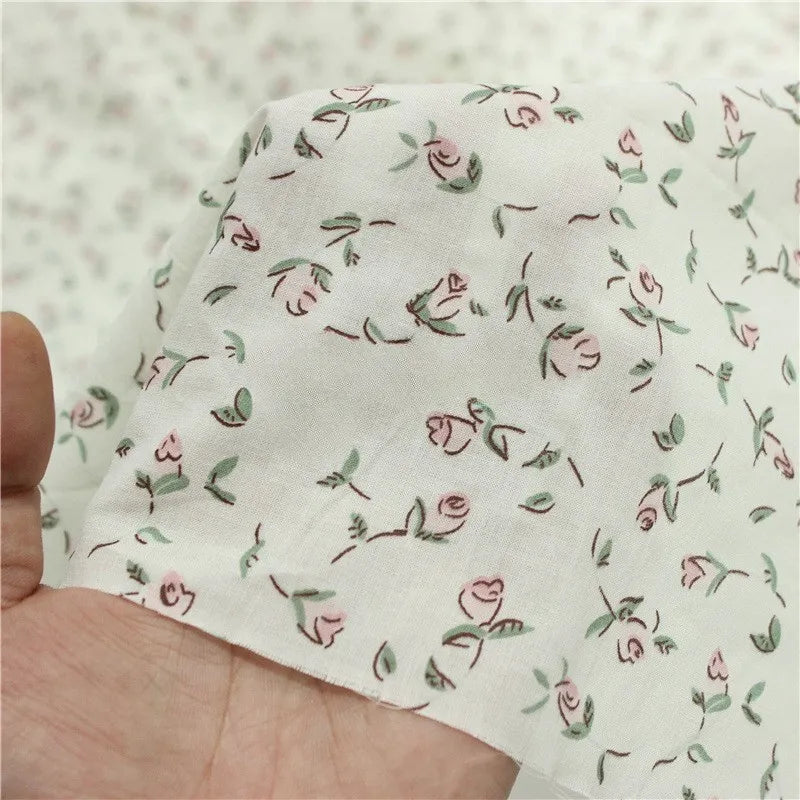 A hand holds Longan Craft's Small Floral Printed Voile Fabric—100% cotton voile by the yard, featuring a soft botanical pattern with pink roses and green leaves, perfect for summer clothing.
