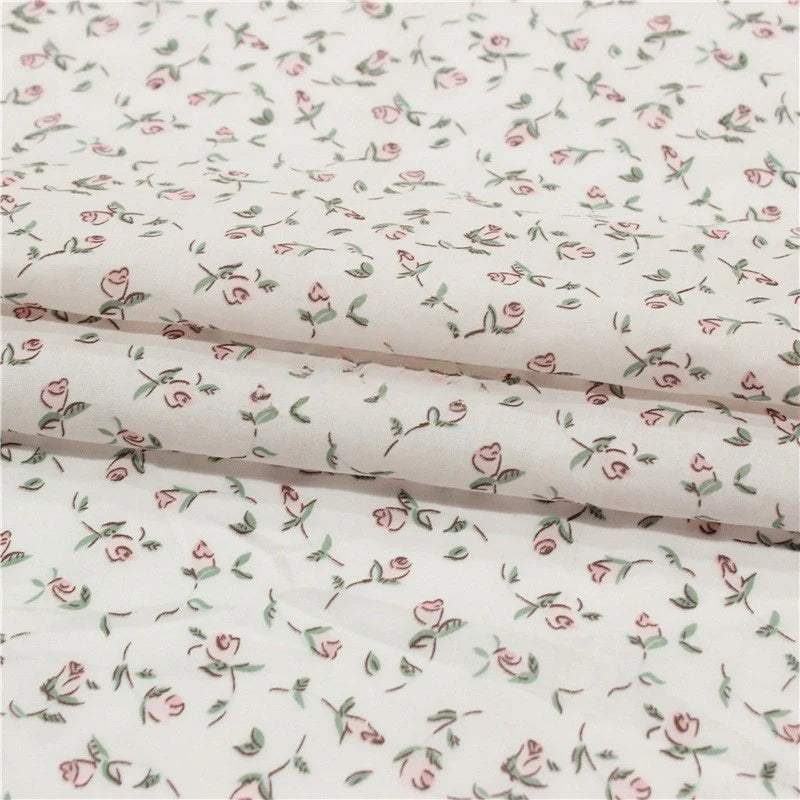 Small Floral Printed Voile Fabric by Longan Craft features soft 100% cotton voile with a botanical pink rose and green leaf pattern, perfect for summer clothing. Shown folded to highlight its lightweight texture. Available by the yard.