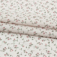 Small Floral Printed Voile Fabric by Longan Craft features soft 100% cotton voile with a botanical pink rose and green leaf pattern, perfect for summer clothing. Shown folded to highlight its lightweight texture. Available by the yard.