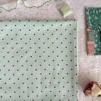 A folded Longan Craft Small Polka Dot Printed Lawn Fabric (100% cotton, pastel green) rests on lace, with green thread, ruffled trim, a floral curtain photo, and a dried rose nearby.