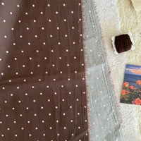 A piece of Longan Craft Small Polka Dot Printed Lawn Fabric, 100% cotton and lightweight, rests beside a dark brown thread spool, lace-like white textile, and a floral seaside card. Ideal for breathable casual garments.