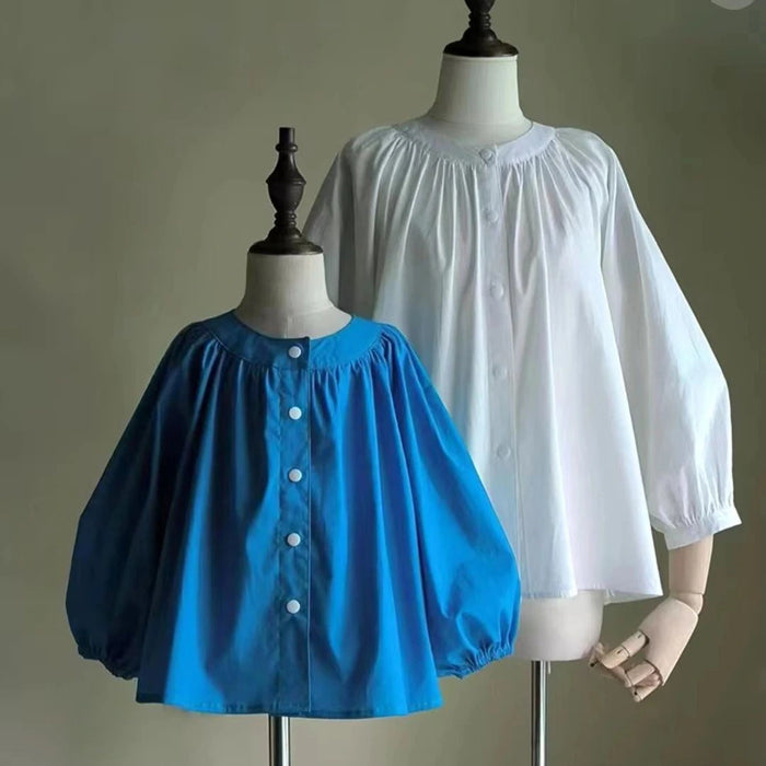 Two mannequins showcase blue and white gathered, long-sleeve blouses with round necklines. Make yours with the Smocked Crewneck Raglan Sleeve Blouse Free Sewing Pattern PDF by Longan Craft.